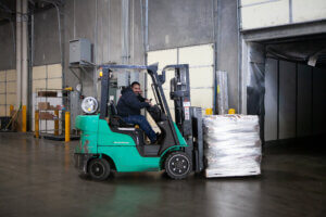 Pallets stacked on a forklift are being brought across a warehouse to the delivery fleet.