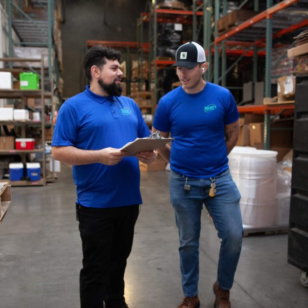 2 men reviewing information on a clipboard in a warehouse preparing packages to be transferred to the delivery fleet