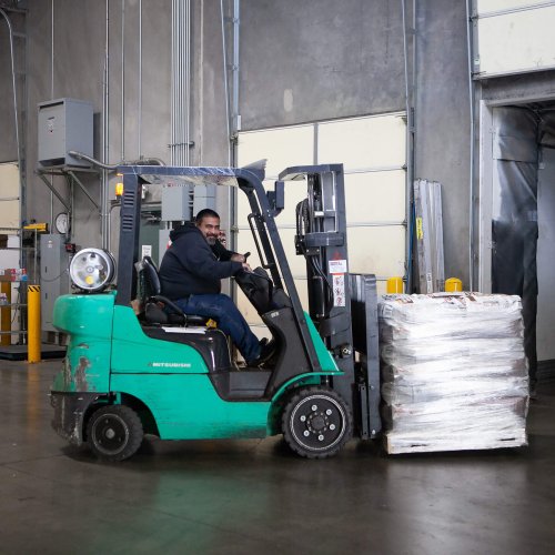 Pallets stacked on a forklift are being brought across a warehouse to the delivery fleet.